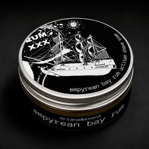 A round tin of Arianah & Evans 'Empyrean Bay' rum, featuring a black and white illustration of a sailing ship on the lid, set against a dark background.